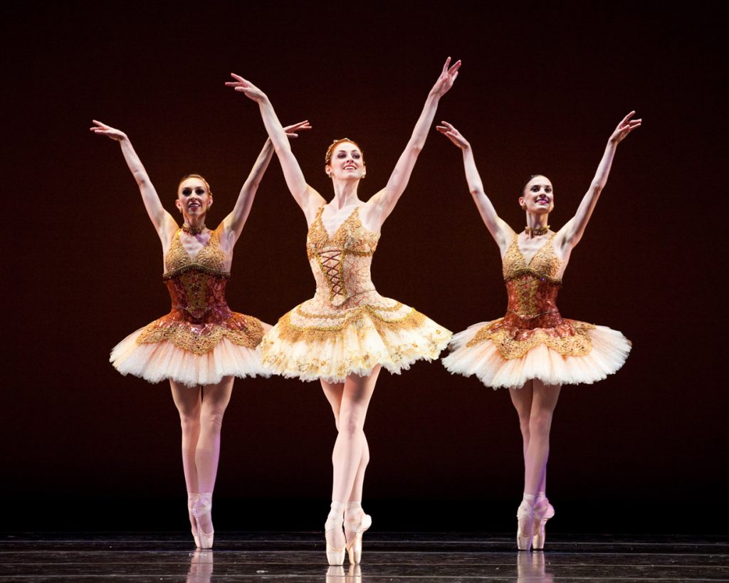 Ballerinas on pointe in red and yellow tutus smiling
