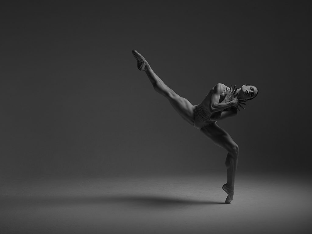 Shelby Williams in a leotard with leg extended to the left, leaning to the right, on pointe on a bent knee. Photo is black and white